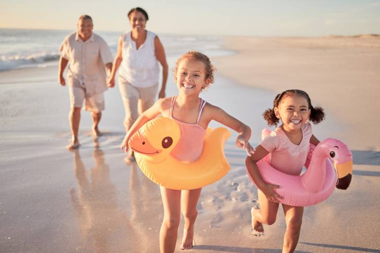 A family with two young children run and play on a beach.