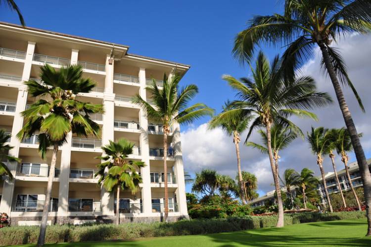 Tall palm trees line the beachfront walking path along Kaanapali Beach in Maui, with luxury oceanfront condos rising on the left.